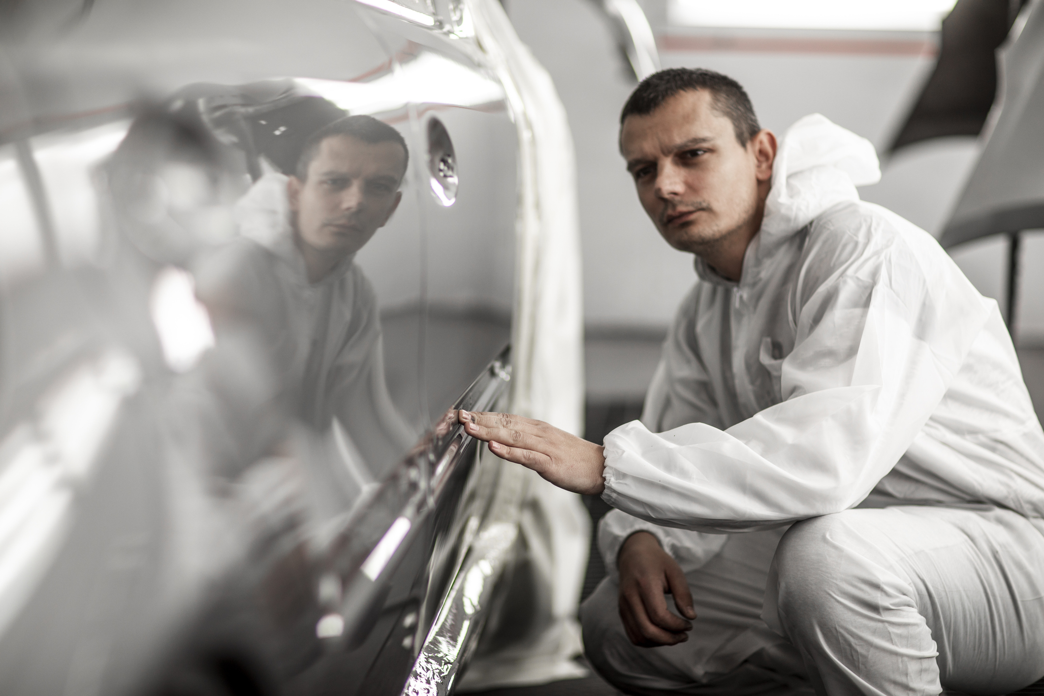 Man inspecting car surface in protective suit.