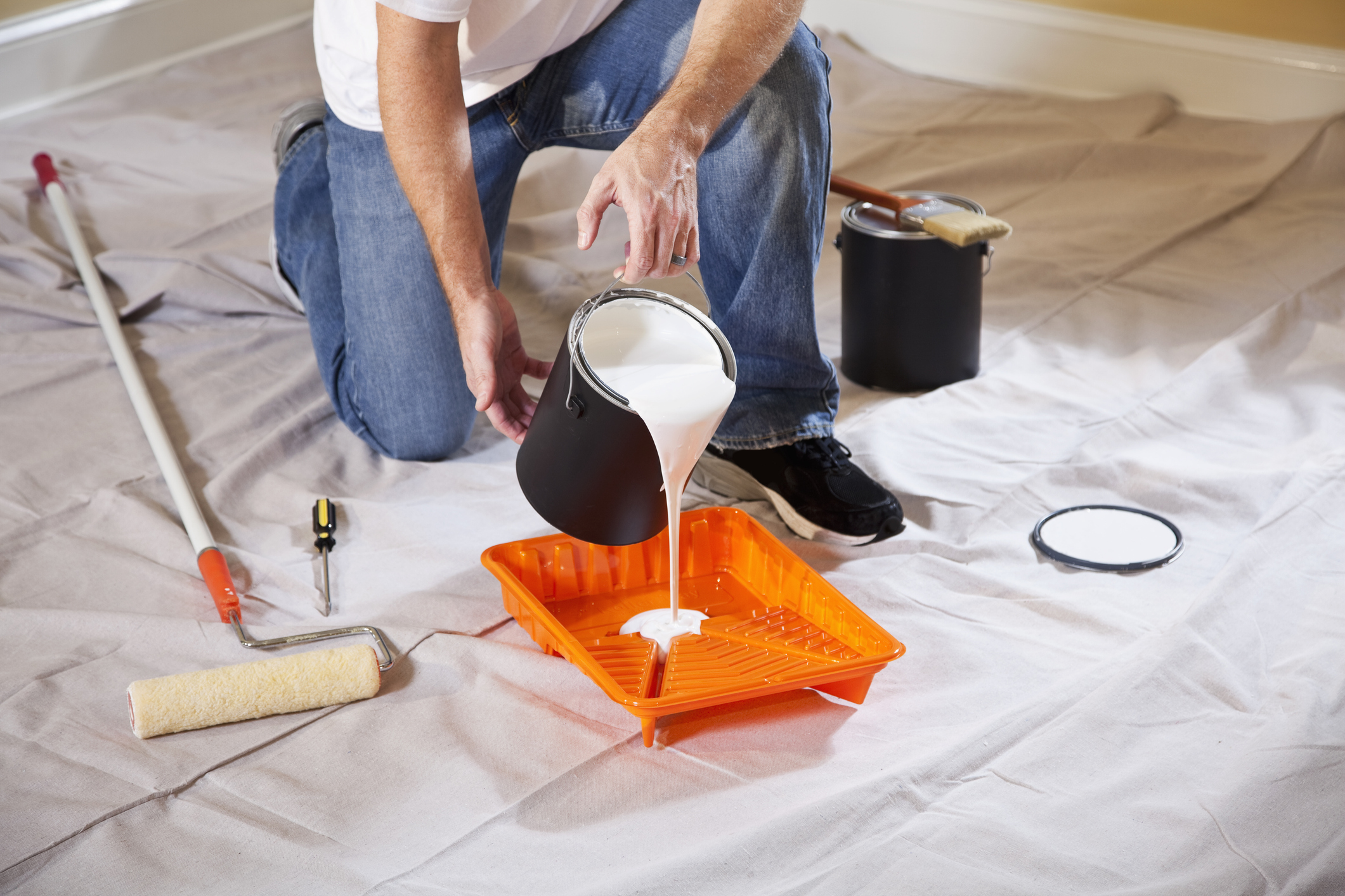 Person pouring white paint into tray.