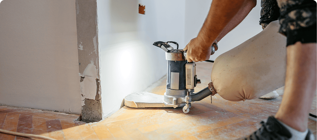Person sanding floor with electric sander tool.