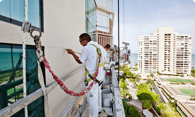 Workers painting building exterior on suspended platform.