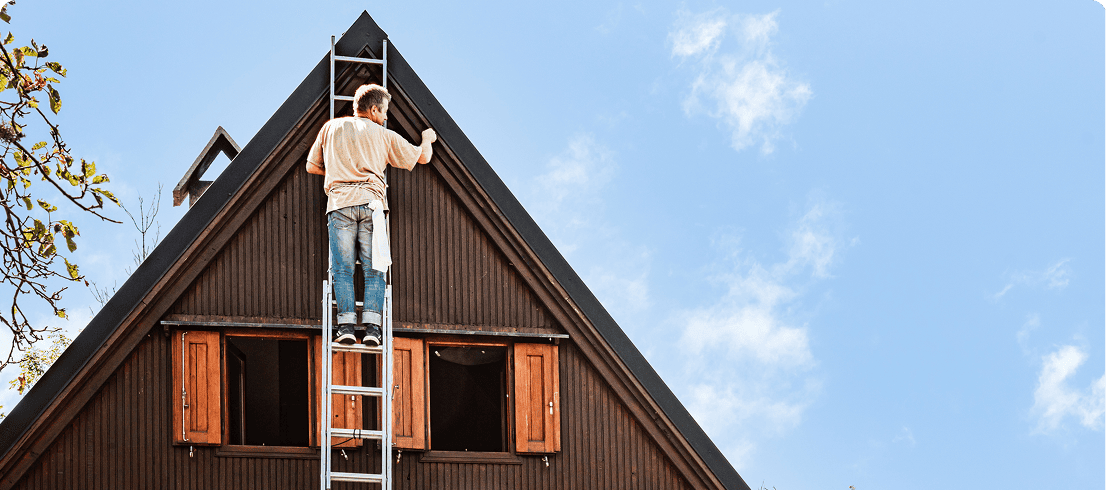 Man on ladder painting wooden house exterior.