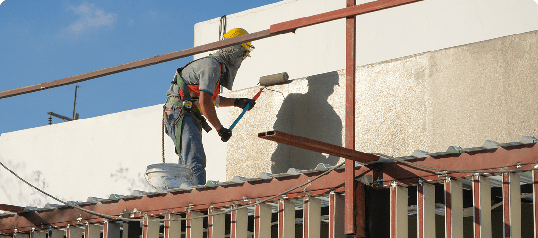Worker painting a building exterior wall.