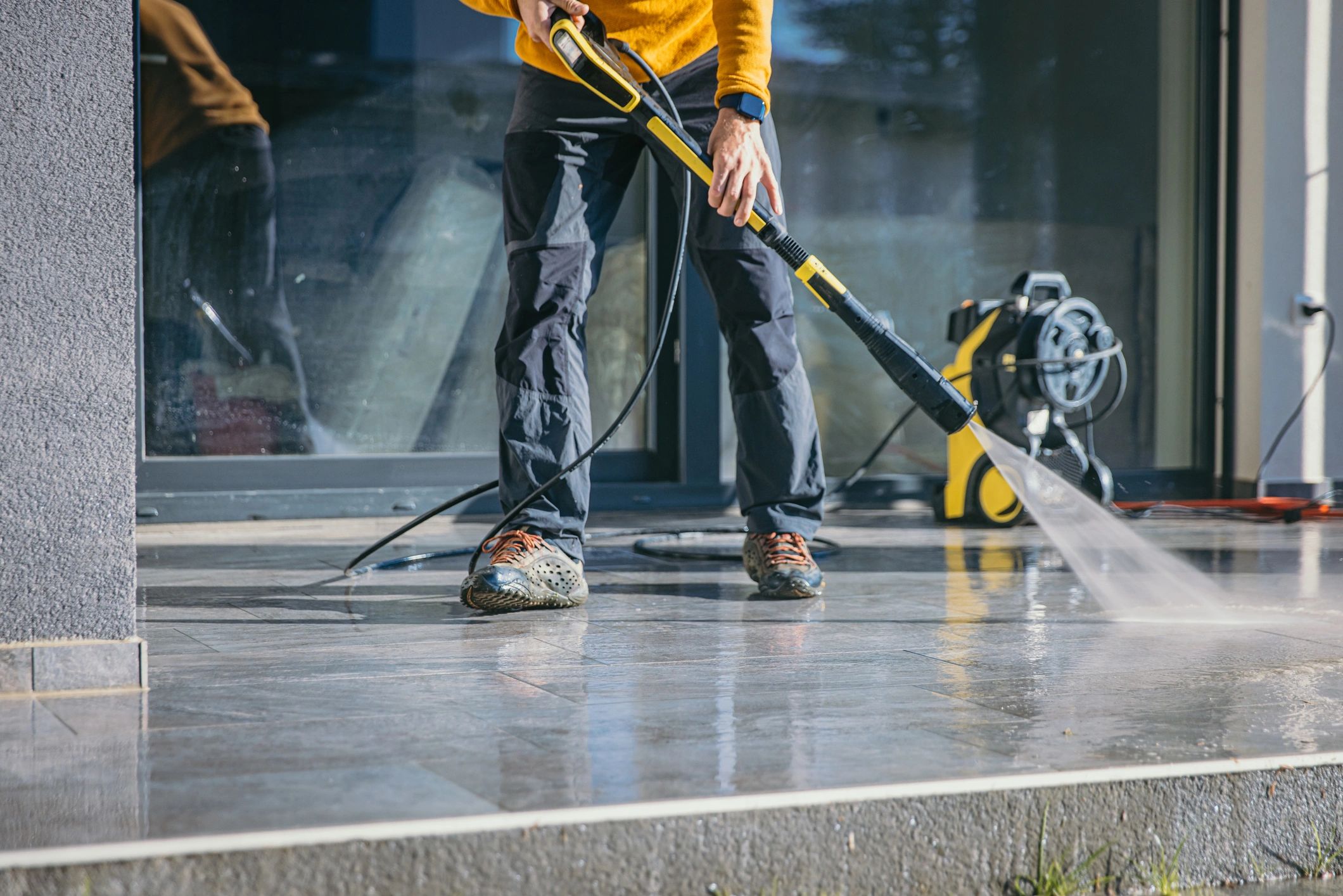 Person pressure washing outdoor patio surface.