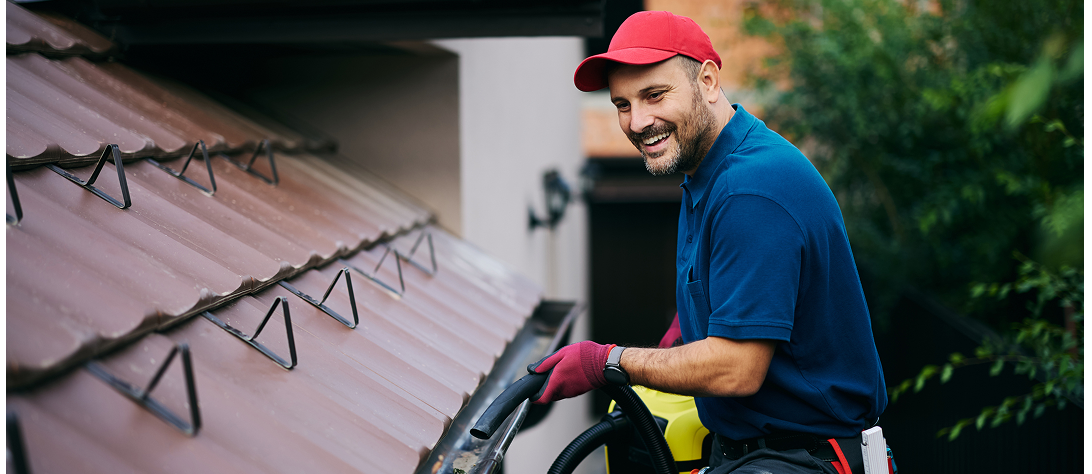 Man cleaning house gutters with vacuum machine.