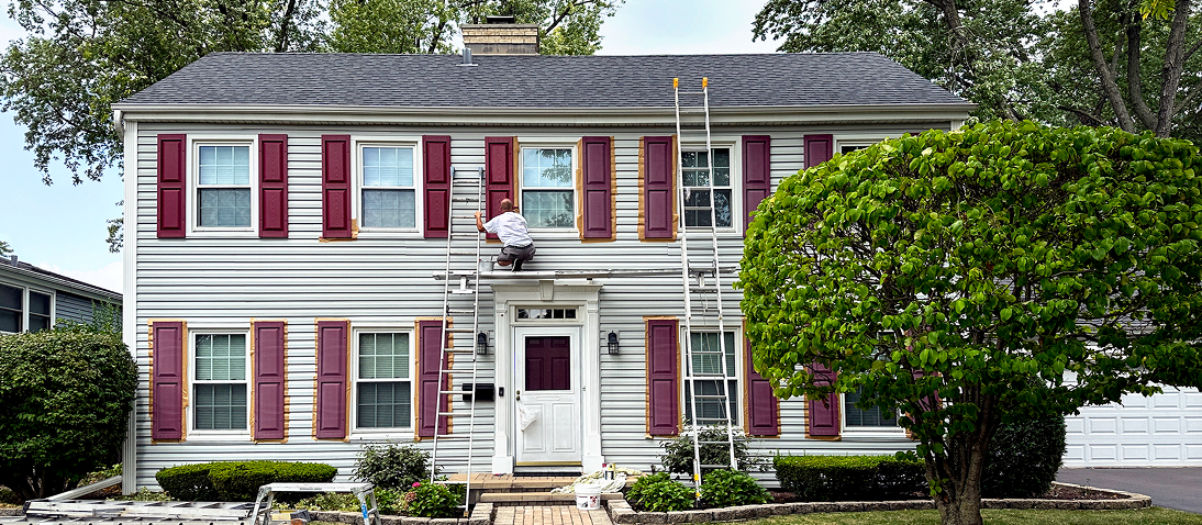 Person painting shutters on a house exterior.