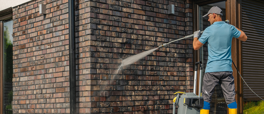 Person pressure washing a brick wall outside.