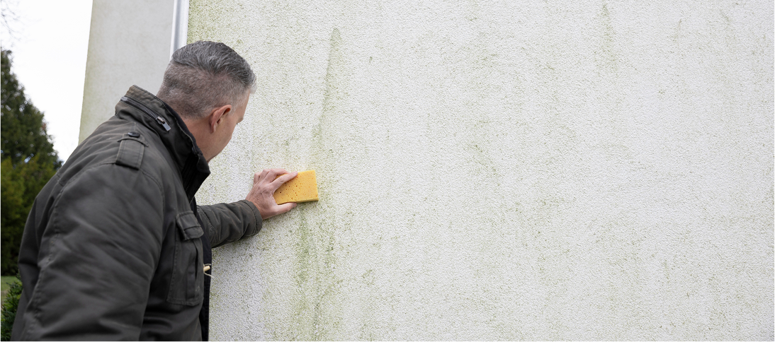 Man cleaning wall with a yellow sponge.