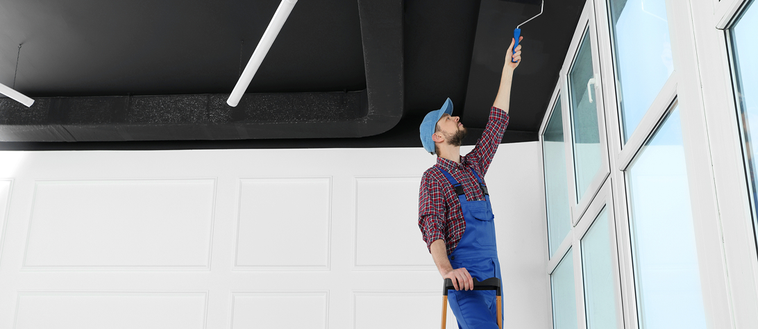 Man painting ceiling with roller on ladder.