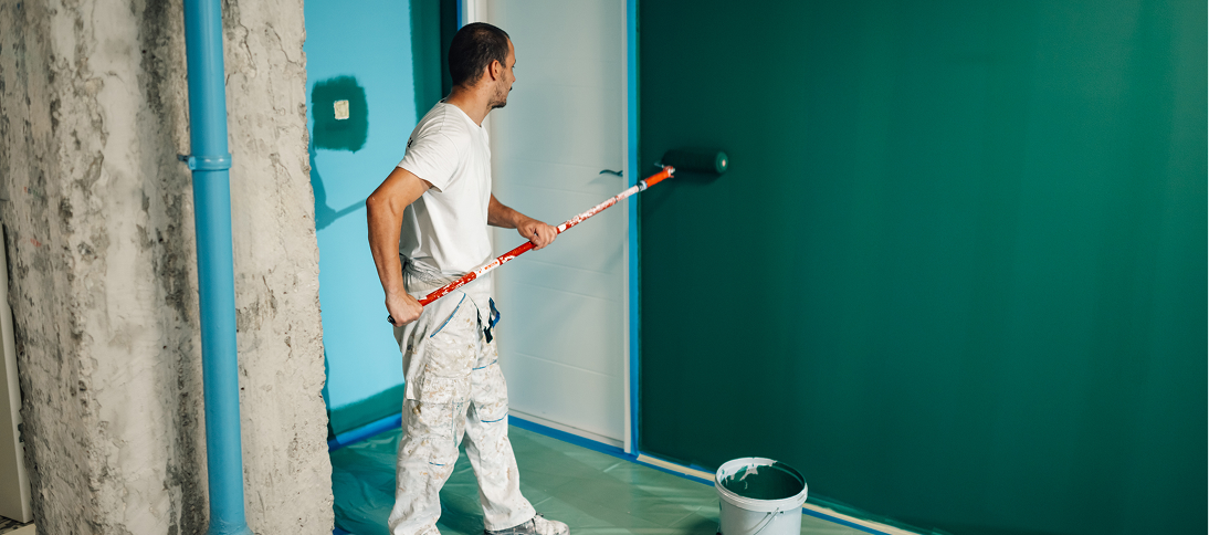 Man painting wall with green paint roller.