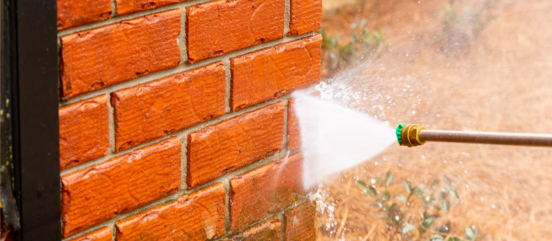 Pressure washing red brick wall with water.