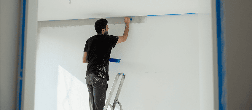 Painter using putty knife on wall while standing on ladder