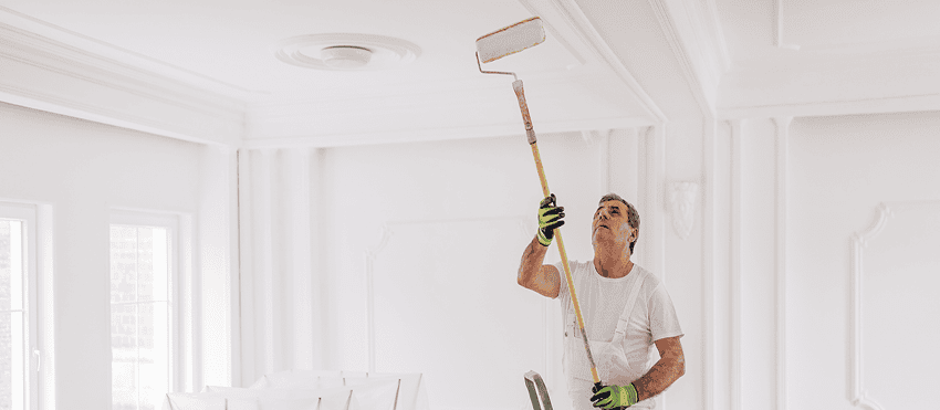 Man painting wall with roller, ladder in background