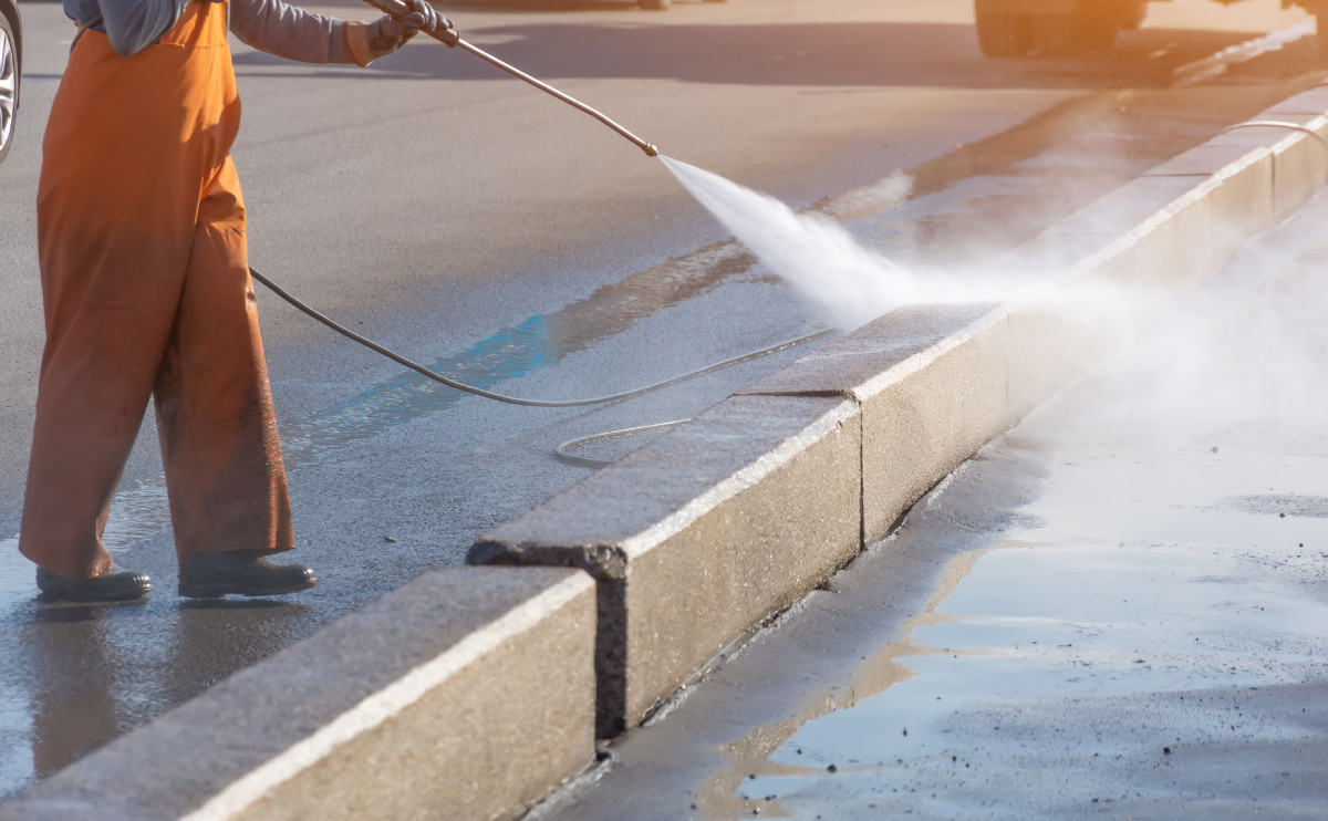 Worker pressure washing pavement