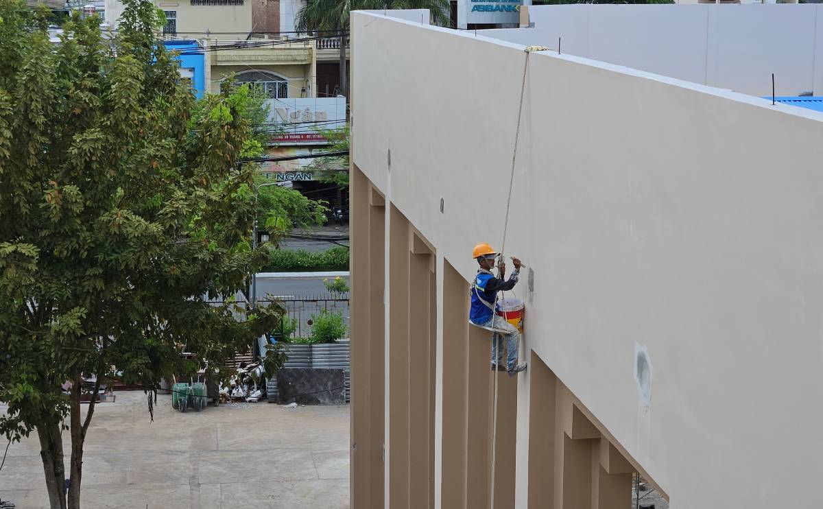 Worker painting tall building wall