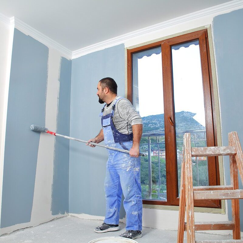 Man painting walls in blue overalls