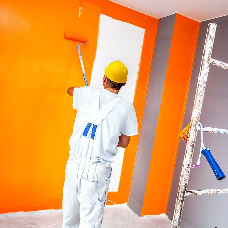 Man in overalls painting interior wall.