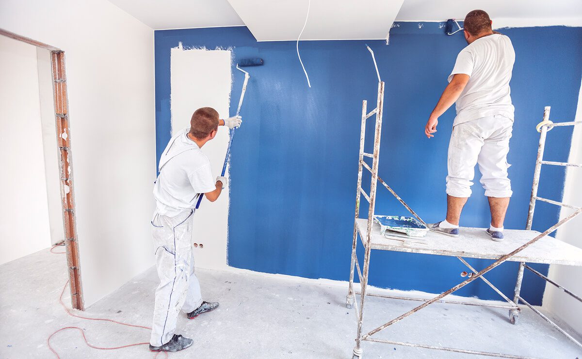 Two painters working on blue wall.