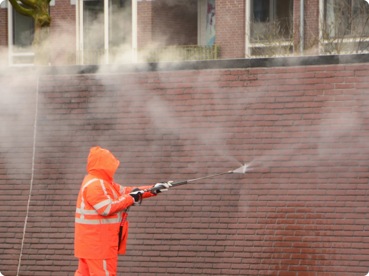 Person cleaning wall with high-pressure hose